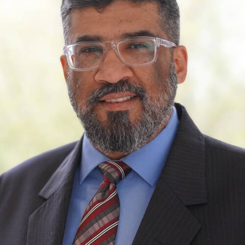 Dr. Samir Iqbal smiling at the camera while wearing a suit in a professional setting.